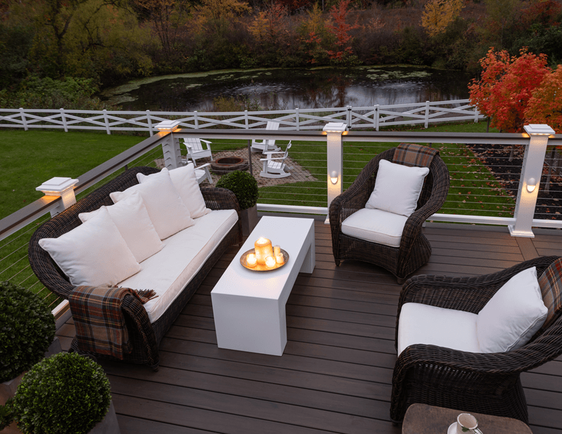 Deck in the evening with steel railing and patio furniture. Lights on the railing and candles on a small table.